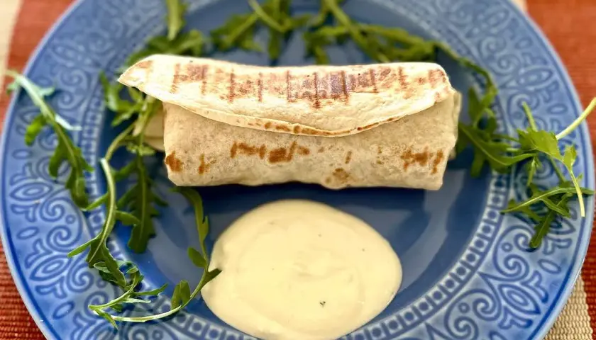 Ciepła tortilla z kurczakiem, podana z sosem i rukolą na niebieskim talerzu. Pyszne danie na szybki obiad.