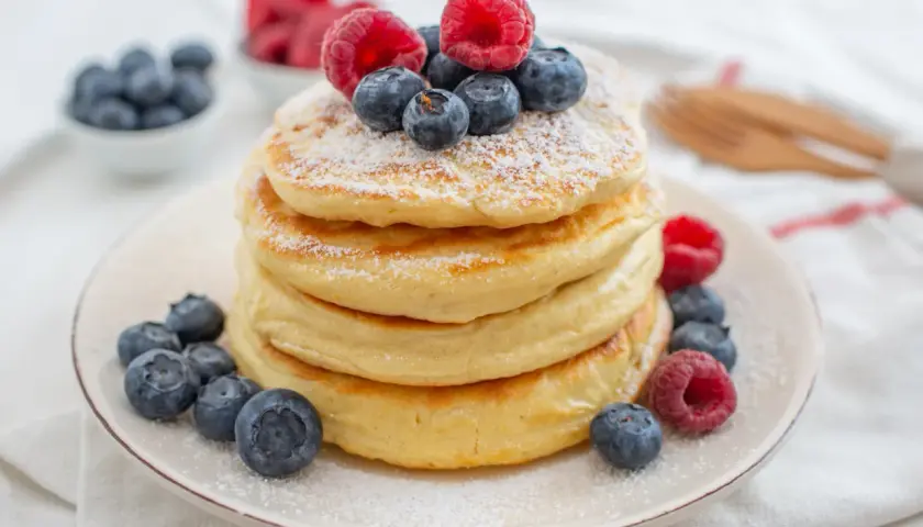 Stos puszystych naleśników z jagodami i malinami, posypanych cukrem pudrem. Czy pancakes są lekkostrawne? Zależy od składników!