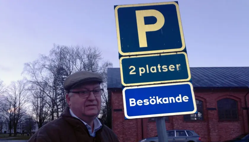 Man i keps vid parkering för personbil klass 2. Skylten visar "2 platser Besökande".