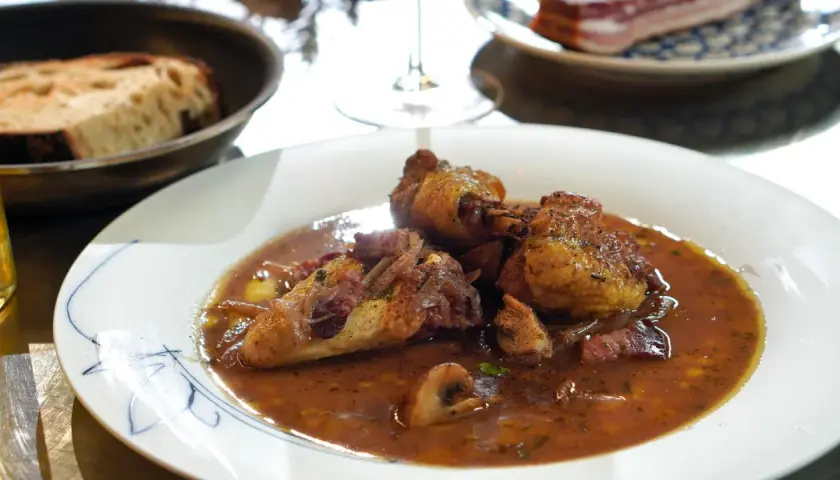 Ein köstliches Coq au Vin Rezept: zartes Hähnchen in Rotwein-Sauce mit Speck und Pilzen, serviert mit Brot.