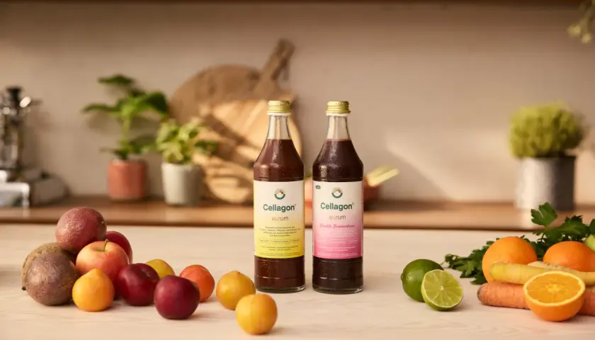 Zwei Flaschen Cellagon Aurum stehen neben frischem Obst und Gemüse. Ideal, um Eisen und Vitamin D zusammen einzunehmen für Vitalität.