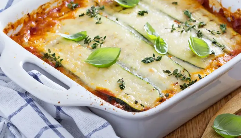 Pyszne lasagne z cukinią, zapieczone pod ciągnącym serem, ozdobione świeżą bazylią i tymiankiem.