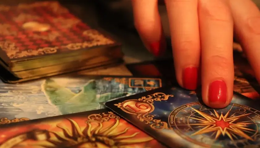 Dłoń z czerwonymi paznokciami nad kartami tarota. Widoczna karta z gwiazdą i znaki zodiaku, sugerująca tarot ryby miesięczny.