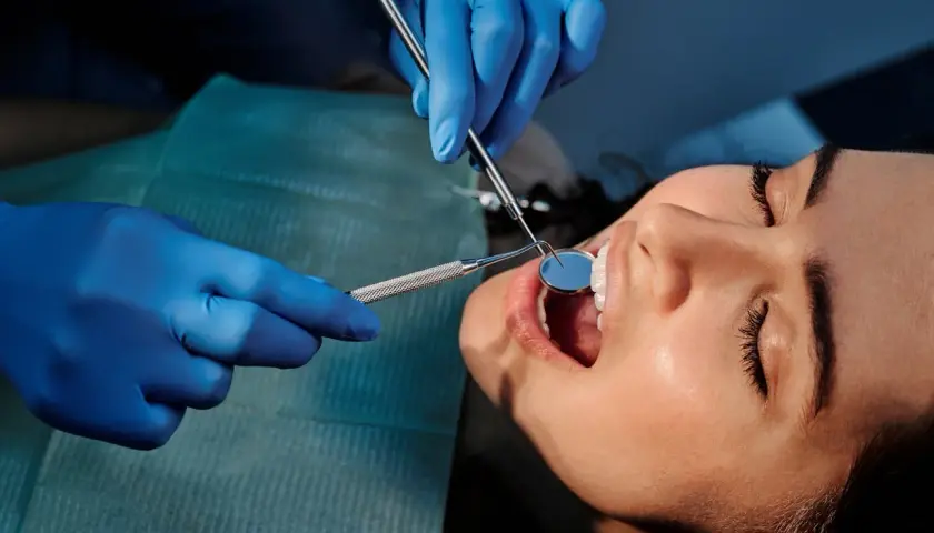 Dentysta bada zęby pacjentki, by wykryć próchnicę. Używa lusterka i narzędzia.