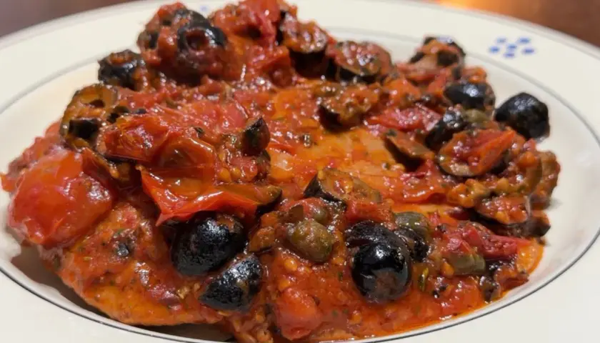 Bistecche alla pizzaiola, un piatto succulento con pomodoro, olive nere e capperi, servito su un piatto bianco con decorazioni blu.