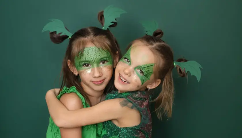 Zwei Mädchen mit Drachenschminke und grünen Flügeln im Haar, ein einfaches Drachen-Kinderschminken-Ergebnis.