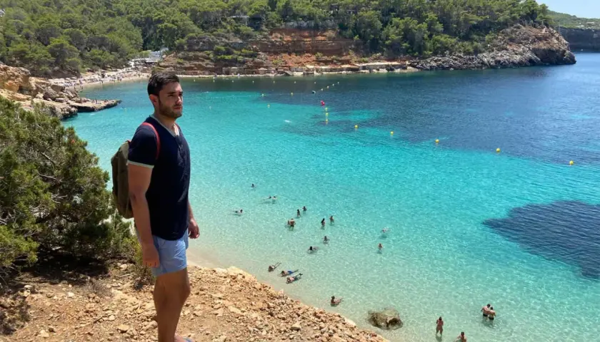 Un hombre con mochila admira una cala turquesa en Ibiza. ¡Un plan perfecto que ver en Ibiza en 4 días!