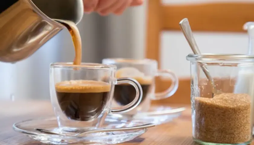 Frisch gebrühter Kaffee wird in ein Glas gegossen. Ob Kaffee den Blutdruck beeinflusst, ist eine häufige Frage. Daneben steht Zucker.