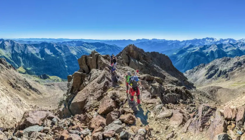 Grupa ludzi wyrusza na trekking po skalistym szczycie, podziwiając rozległe pasmo górskie w oddali.
