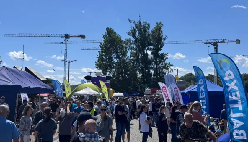 Tłum ludzi na zewnątrz, namioty, flagi i dźwigi w tle.