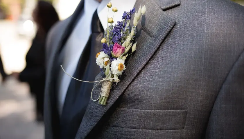 Elegancka, szara marynarka z czarnym krawatem i delikatną, suszoną butonierką z lawendą i białymi kwiatkami.