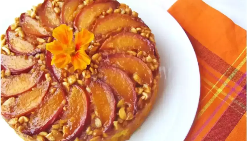 Deliziosa torta di pesche rovesciata, con pesche caramellate, noci croccanti e un fiore arancione al centro.