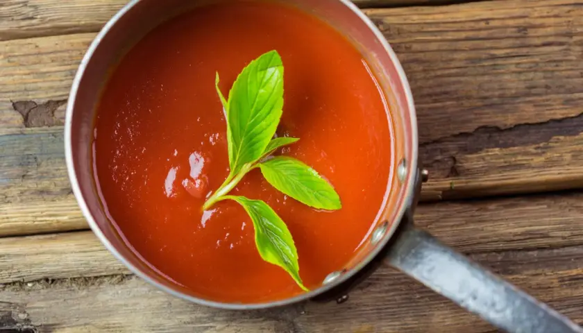 Frische, hausgemachte tomatensauce aus reifen Tomaten, garniert mit Basilikum, in einem Topf auf rustikalem Holz.