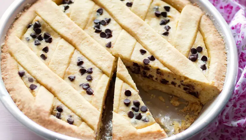 Deliziosa crostata ricotta e gocce di cioccolato, con una fetta tagliata per mostrare il ripieno cremoso e le gocce scure.