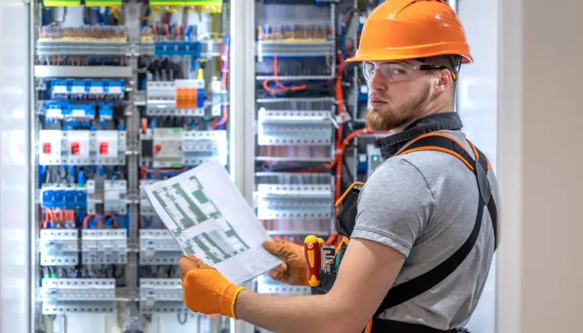 Elektryk z uprawnieniami SEP G1 sprawdza schemat przy rozdzielnicy elektrycznej.