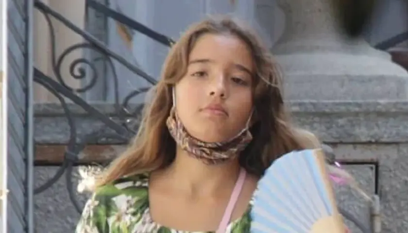 Léonie Cassel, z wachlarzem w ręku i maseczką na szyi, w kwiecistej sukience.