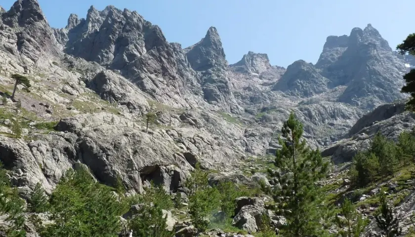 Skaliste zbocza górskie z sosnami, prowadzące ku szczytom. Widok na najwyższy szczyt Korsyki, Monte Cinto, w słoneczny dzień.