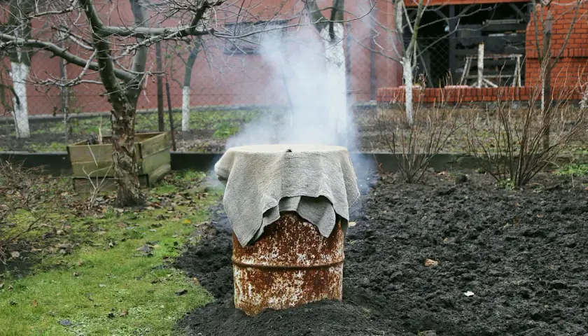 Dym unosi się z rustykalnej wędzarni z beczki, która stoi na ziemi w ogrodzie.