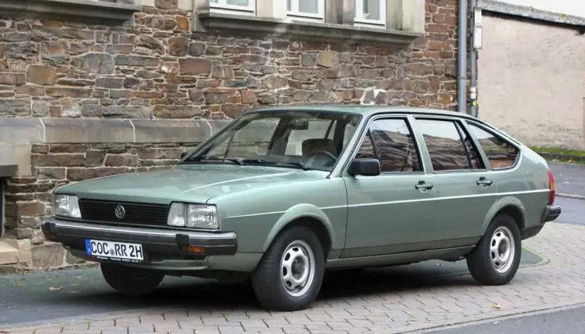 Zielonawy Volkswagen Passat, klasyk z lat 80., parkuje przed kamiennym budynkiem.