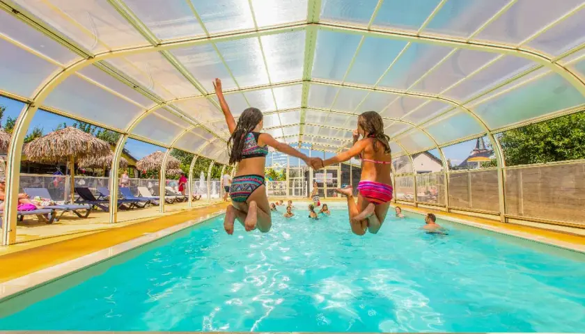 Deux filles sautent main dans la main dans une piscine couverte. Vacances en camping-car à Saint-Malo.