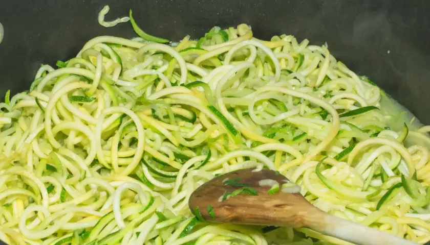 Makaron z cukinii w patelni, mieszany drewnianą łyżką. Zdrowy i lekki posiłek w przygotowaniu.
