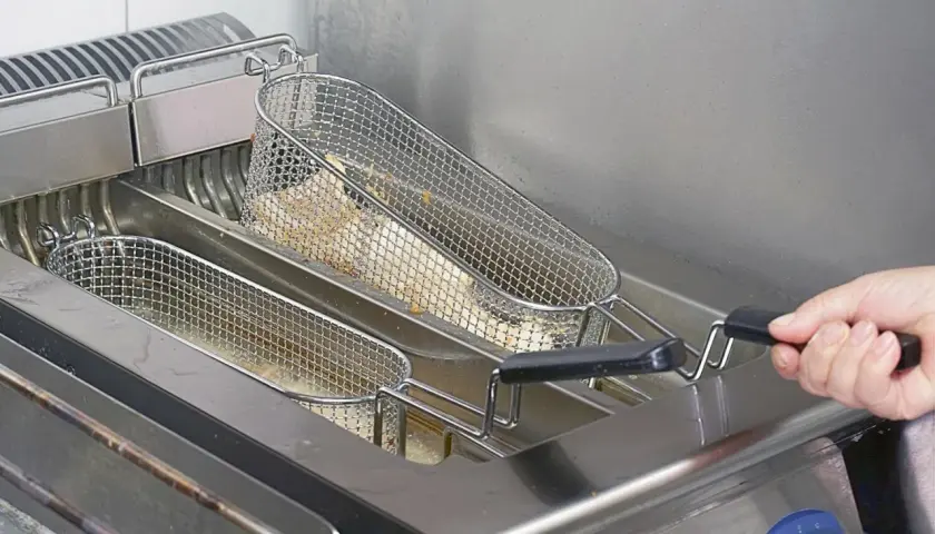 Frytki smażące się w metalowych koszach we frytkownicy.
