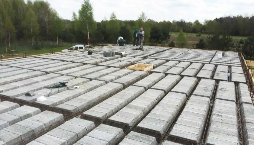 Budowa stropu teriva w toku. Betonowe pustaki ułożone w rzędach, zbrojenie gotowe do zalania. Pracownicy doglądają postępu prac.