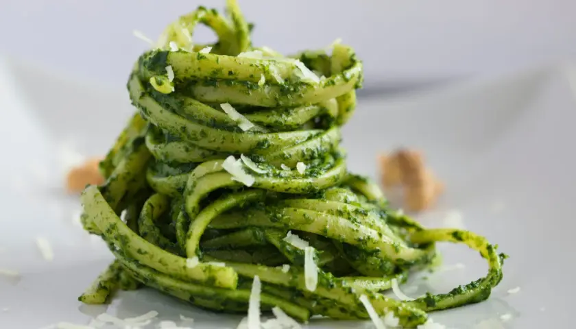 Makaron tagliatelle z zielonym pesto bazyliowym i startym parmezanem na białym talerzu.