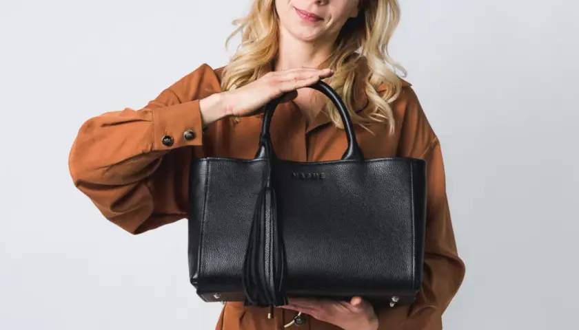 Elegancka, czarna torebka z frędzlem, idealna jako modne torebki na lato. Kobieta w rudym kombinezonie prezentuje stylowy dodatek.