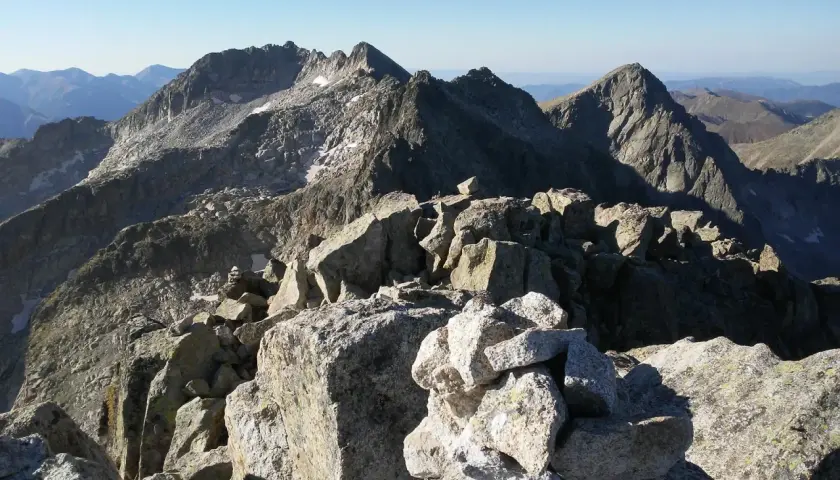 Cumbre rocosa con cairn, vista panorámica de montañas escarpadas bajo cielo azul. Besiberri Nord.