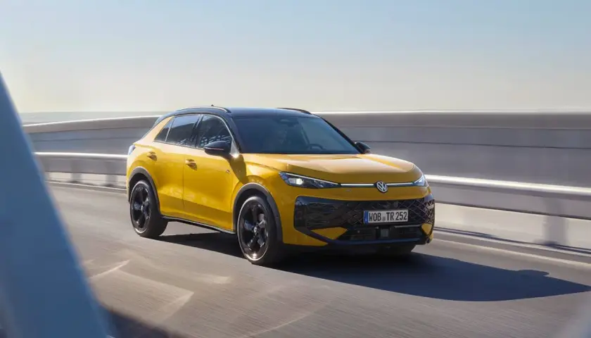 Żółty Volkswagen Cross pędzi po drodze, błyszcząc w słońcu.
