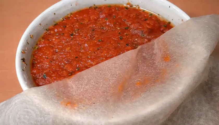 Un tazón blanco con la mejor salsa de tomate para pizza, con hierbas y un trozo de papel de arroz.