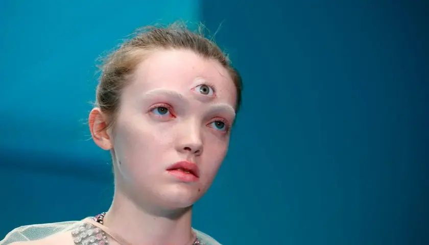 Modelka z trzecim okiem na czole, jakby otwierała się jej szyszynka. Jasna skóra, białe brwi, niebieskie oczy.