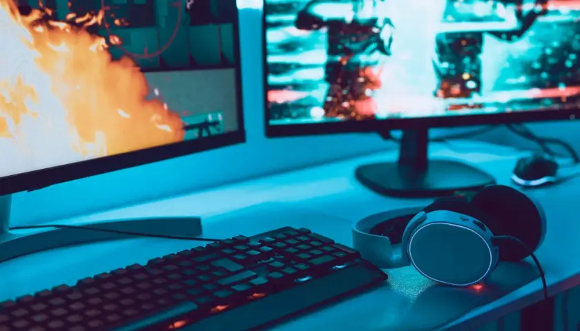 Gaming-Setup mit zwei Monitoren, Tastatur und Kopfhörern. Auf dem linken Bildschirm lodert Feuer, rechts sind Charaktere zu sehen. Perfekt für VA oder IPS.