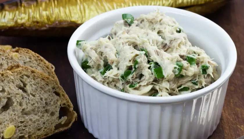 Pyszna pasta z makreli i twarogu, posypana szczypiorkiem, obok kromek chleba i wędzonej makreli.