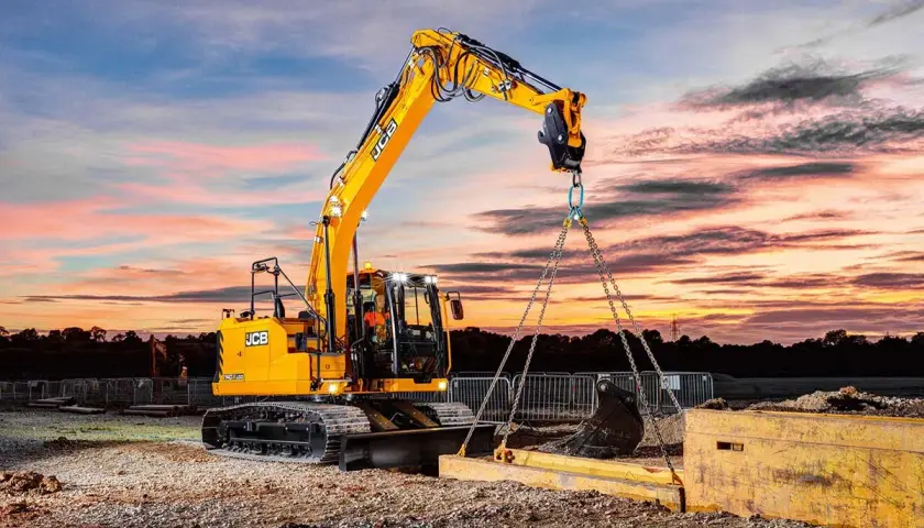 Operator koparki kurs: żółta maszyna JCB podnosi ciężki element na tle zachodzącego słońca.