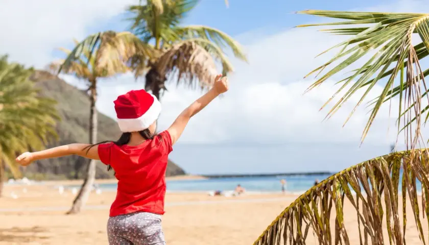 Dziewczynka w czapce Mikołaja cieszy się plażą i palmami. To wyjątkowe boże narodzenie w ciepłych krajach, gdzie śnieg zastępuje piasek.