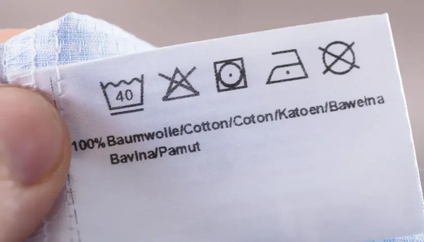 Pflegeetikett mit Waschsymbolen. Das Trockner Symbol ist durchgestrichen, was bedeutet, dass das Kleidungsstück nicht im Trockner getrocknet werden darf.