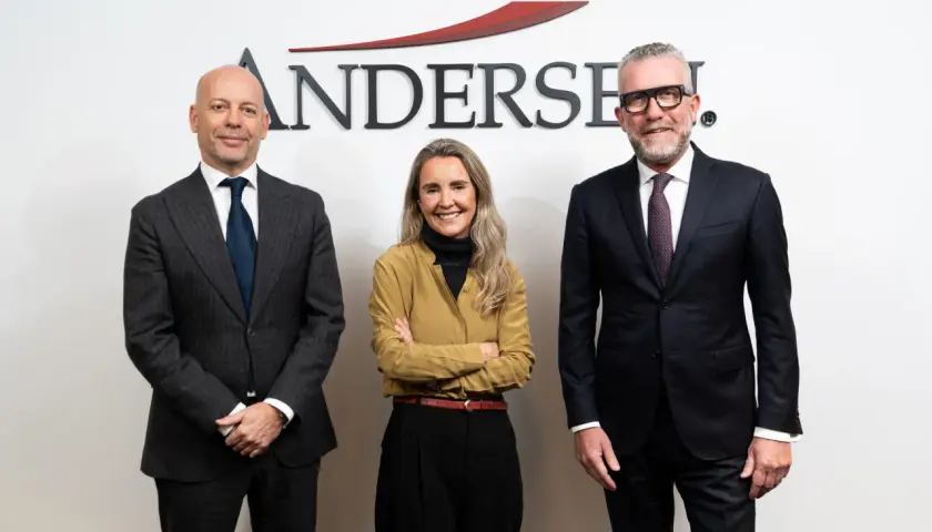 Tres personas posan frente al logo de Andersen. El hombre de la izquierda, calvo, viste traje gris. La mujer del centro, con brazos cruzados, lleva una blusa ocre. El hombre de la derecha, con gafas, viste traje oscuro. Un momento clave, como un ejempl...