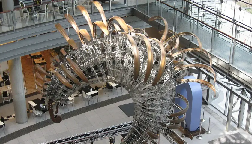 Duża, metalowa rzeźba przypominająca szkielet dinozaura w centrum handlowym.