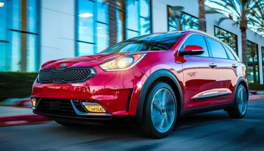 Czerwony Kia Niro Hybrid w ruchu, z palmami i nowoczesnym budynkiem w tle.