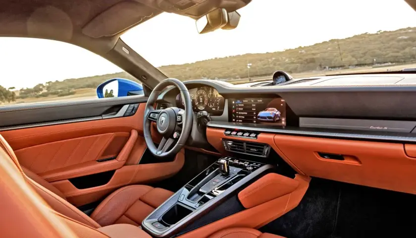 Wnętrze Porsche 911 GTS w kolorze pomarańczowym, z nowoczesnym kokpitem i ekranem multimedialnym.