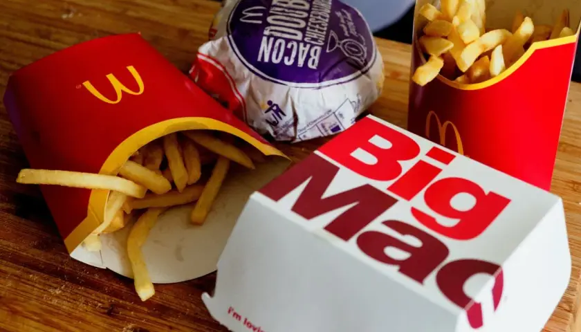 Frytki z McDonald's w czerwonych opakowaniach obok pudełka Big Mac i burgera.