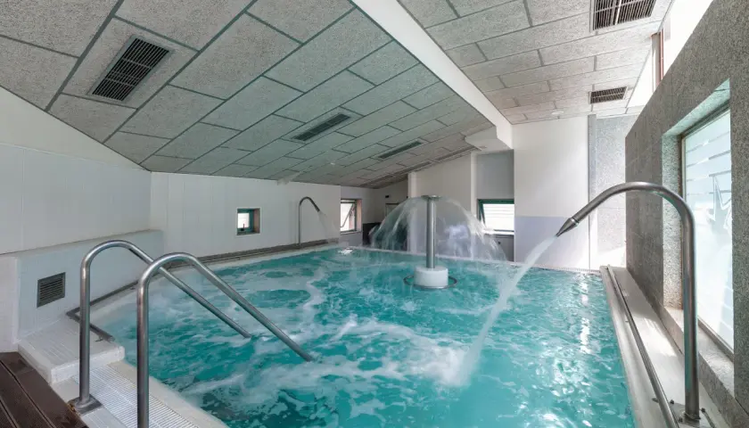 Piscina de hidromasaje con chorros de agua y cascada central en un balneario.