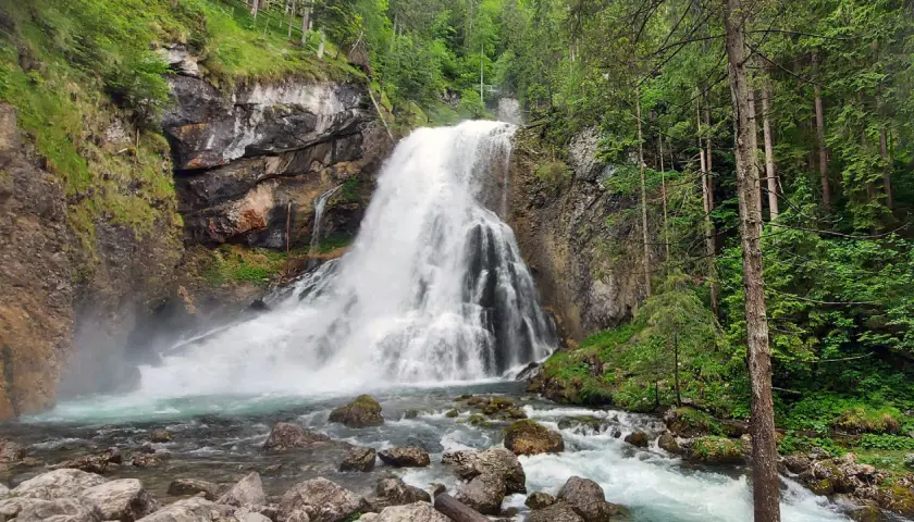 Tosender Wasserfall im Teutoburger Wald, umgeben von Felsen und üppigem Grün. Das Wasser stürzt tosend in ein türkisfarbenes Becken.