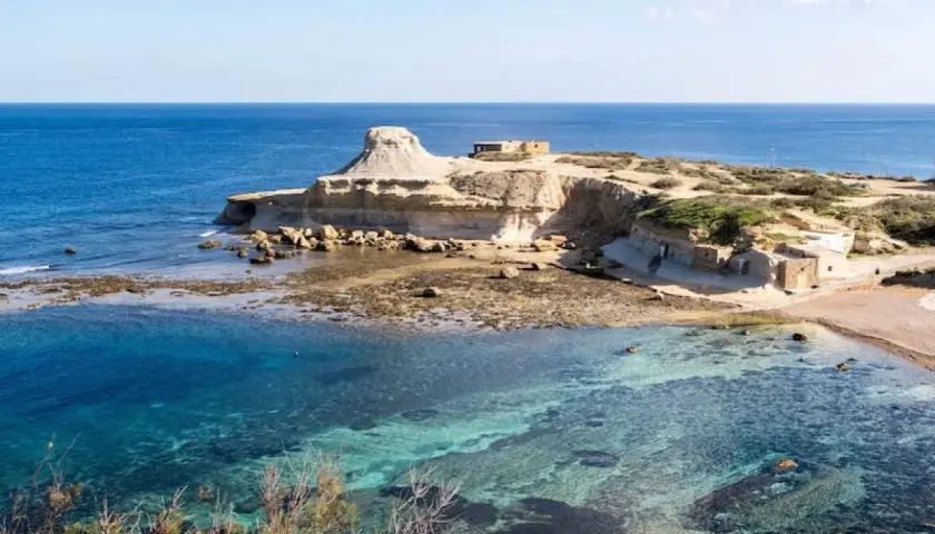Felsige Küste mit kristallklarem Wasser und kleinen Gebäuden auf der Insel Gozo.