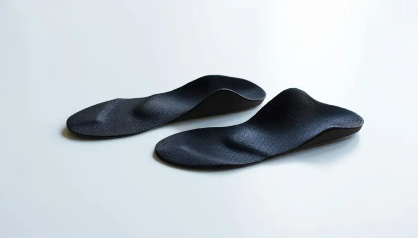 Zwei schwarze, ergonomisch geformte sensomotorische Schuheinlagen liegen auf weißem Untergrund.