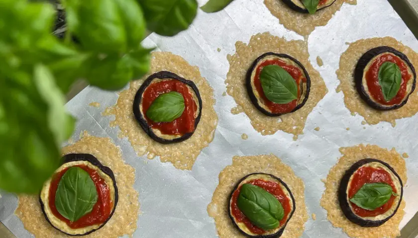 Kleine Aubergine-Pizza-Häppchen mit Tomatensoße, Käse und frischem Basilikum auf einem Backblech.