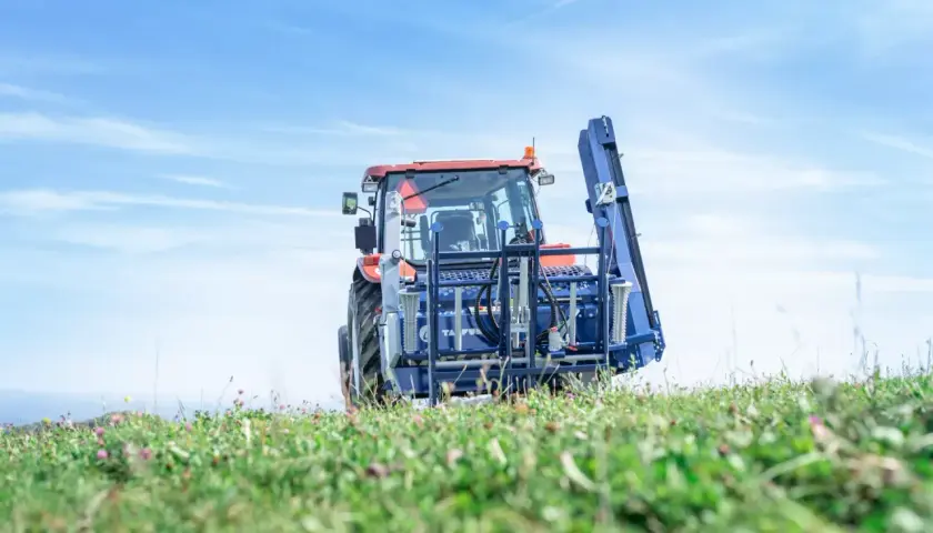 Traktor mit Tajfun RCA 480 auf einem grünen Feld unter blauem Himmel.