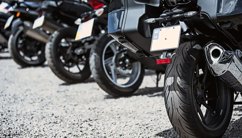 Varias motos aparcadas en fila, una moto sin matrícula visible en primer plano, con su rueda trasera y maleta.
